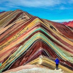 a man standing on top of a mountain next to a rainbow colored slope in the mountains