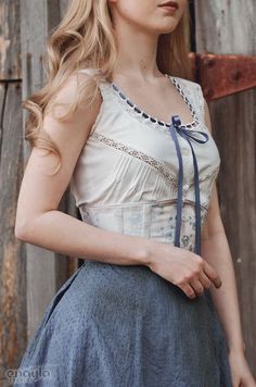 a woman with long blonde hair wearing a white top and blue skirt standing in front of a wooden fence