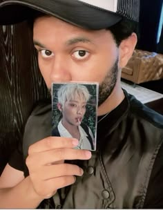 a man holding up a photo of himself in front of his face and wearing a hat