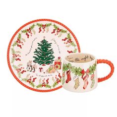 a cup and saucer with a christmas tree design on the side, sitting next to each other