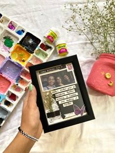 a person holding up a framed photo in front of some crafting supplies