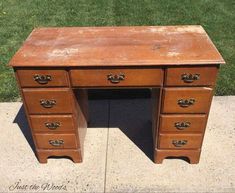 an old wooden desk sitting on the side of a sidewalk with grass in the background