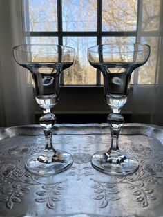 two glass goblets sitting on top of a metal tray in front of a window