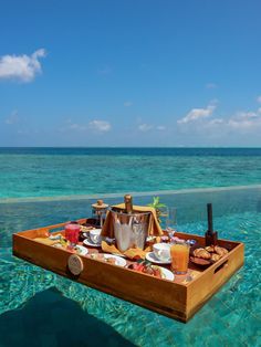 a wooden boat floating in the ocean with food and drinks on it's tray