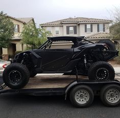 a black vehicle is on the back of a flatbed trailer in front of a house