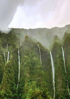 the waterfall is surrounded by green trees and mountains