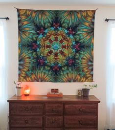 a room with a large tapestry hanging on the wall next to a dresser and window