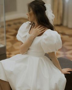 a woman in a white dress sitting on a chair with her hands behind her neck