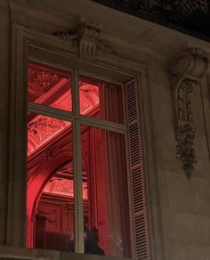 an open window with red light shining through it's glass panes and ornate carvings