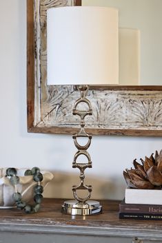 a lamp sitting on top of a wooden table next to a mirror and pine cones