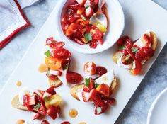 a white plate topped with fruit salad next to a bowl of sauce and a fork