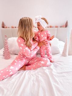 a woman holding a baby in her arms while sitting on top of a white bed