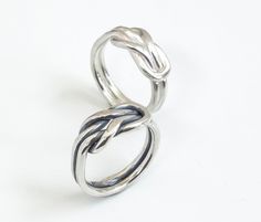 two silver rings on a white surface with one ring twisted in the middle and another knoted at the end