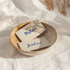 two paper signs are in a bowl on the snow covered ground with dried grass behind them