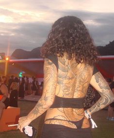 a woman with tattoos on her back standing in front of other people at an outdoor event