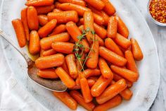 a plate full of baby carrots with a spoon in it and some seasoning on the side