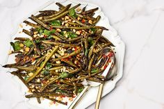 a white plate topped with green beans and other food on top of a marble table