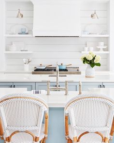 two wicker chairs sit in front of a white kitchen island with open shelving