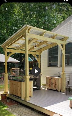 a wooden gazebo sitting on top of a patio next to a building with a grill