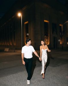 a man and woman holding hands while walking down the street in front of a building