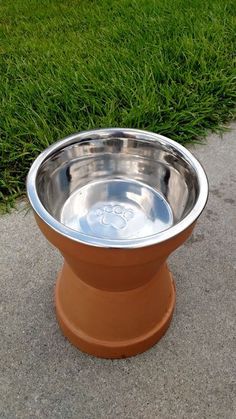 a metal bowl sitting on top of a sidewalk next to green grass in the background