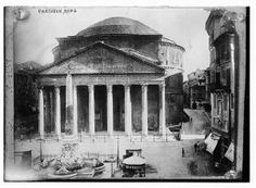 an old black and white photo of a building with columns on the front, surrounded by other buildings