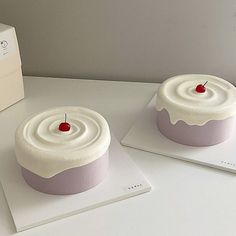 two cakes with white frosting and a cherry on top are sitting on the counter