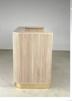 a wooden trash can sitting on top of a cement floor next to a white wall