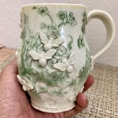 a hand holding a green and white coffee cup with flowers on the outside of it