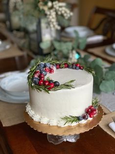 a white cake topped with berries and greenery on top of a wooden table next to plates