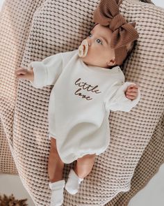 a baby laying on top of a bed next to a teddy bear wearing a brown bow