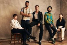 four men sitting on chairs in front of a wall with their arms crossed and looking at the camera