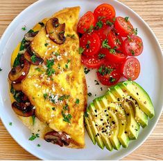 an omelet with mushrooms, tomatoes and avocado on a white plate