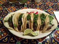 three tacos on a plate with lime wedges and garnished cilantro