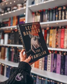 a person holding up a book in front of a bookshelf full of books