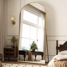 a large mirror sitting on top of a bed next to a dresser and window in a bedroom