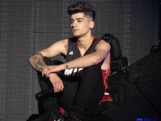 a young man sitting on top of a chair in front of a wall wearing a jersey