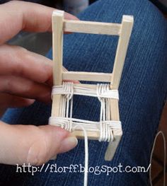 someone is holding a miniature chair made out of string and wood sticks with yarn on it