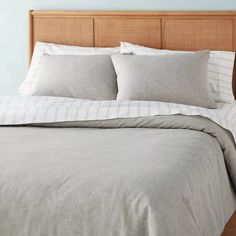 a bed with white and grey linens in a blue room, next to a wooden headboard