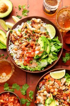 two bowls filled with food next to beer and avocado slices on the table