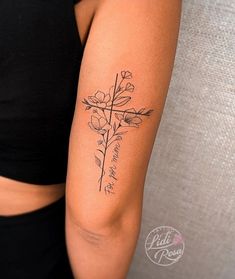 a woman's arm with a cross and flowers tattoo on the left side of her arm