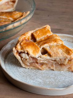 a slice of apple pie on a plate next to a glass bowl with another pie in the background