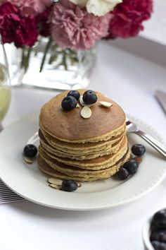 a stack of pancakes with blueberries and almonds on a plate next to flowers