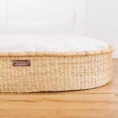 a wicker dog bed with a white pillow on the bottom and brown leather label