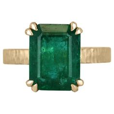 This 4.45-carat natural emerald cut emerald from Zambia is a showstopper. The emerald is cut in a classic emerald cut style, which shows off the stone's clarity and depth of color. The emerald is set in a unique four-double claw prong setting, which adds a modern twist to the classic style. The band of the ring is finished in matte hammered gold in 18K, which gives it a rustic and organic feel. The gold finish provides a beautiful contrast to the deep green of the emerald and adds a touch of war Solitaire Setting, Claw Prong, Hammered Gold, Yellow Gold Setting, Zambia, Natural Emerald, Deep Green, Solitaire Ring, Emerald Cut