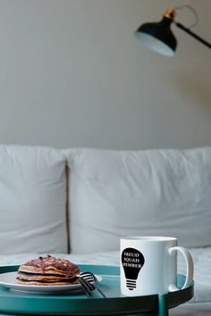 a breakfast tray with pancakes, coffee mug and lamp on the bed in a hotel room