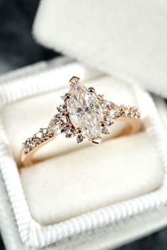 an engagement ring in a white box with diamonds on the band and side stones at the top