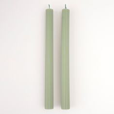 two green candles sitting next to each other on a white surface with one candle in the middle