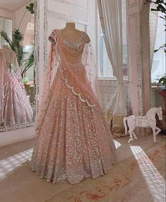 an elaborate pink gown is displayed in front of a mirror with other dresses on display