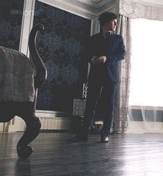 a man standing in front of a window next to a chair and wall with curtains